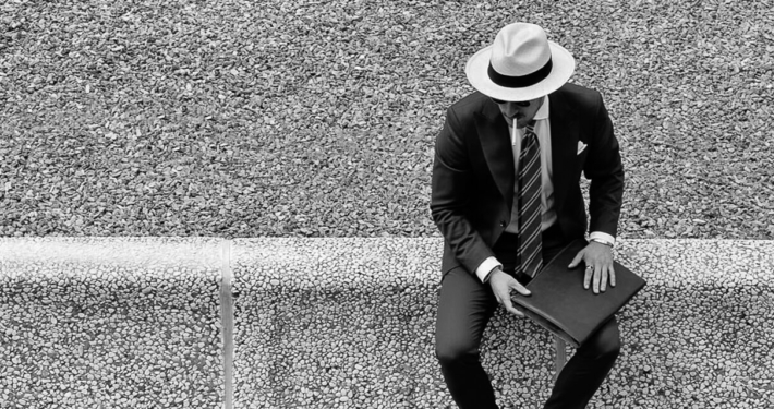 A visitor to the Pitti Uomo sitting on a wall, smoking a cigarette.